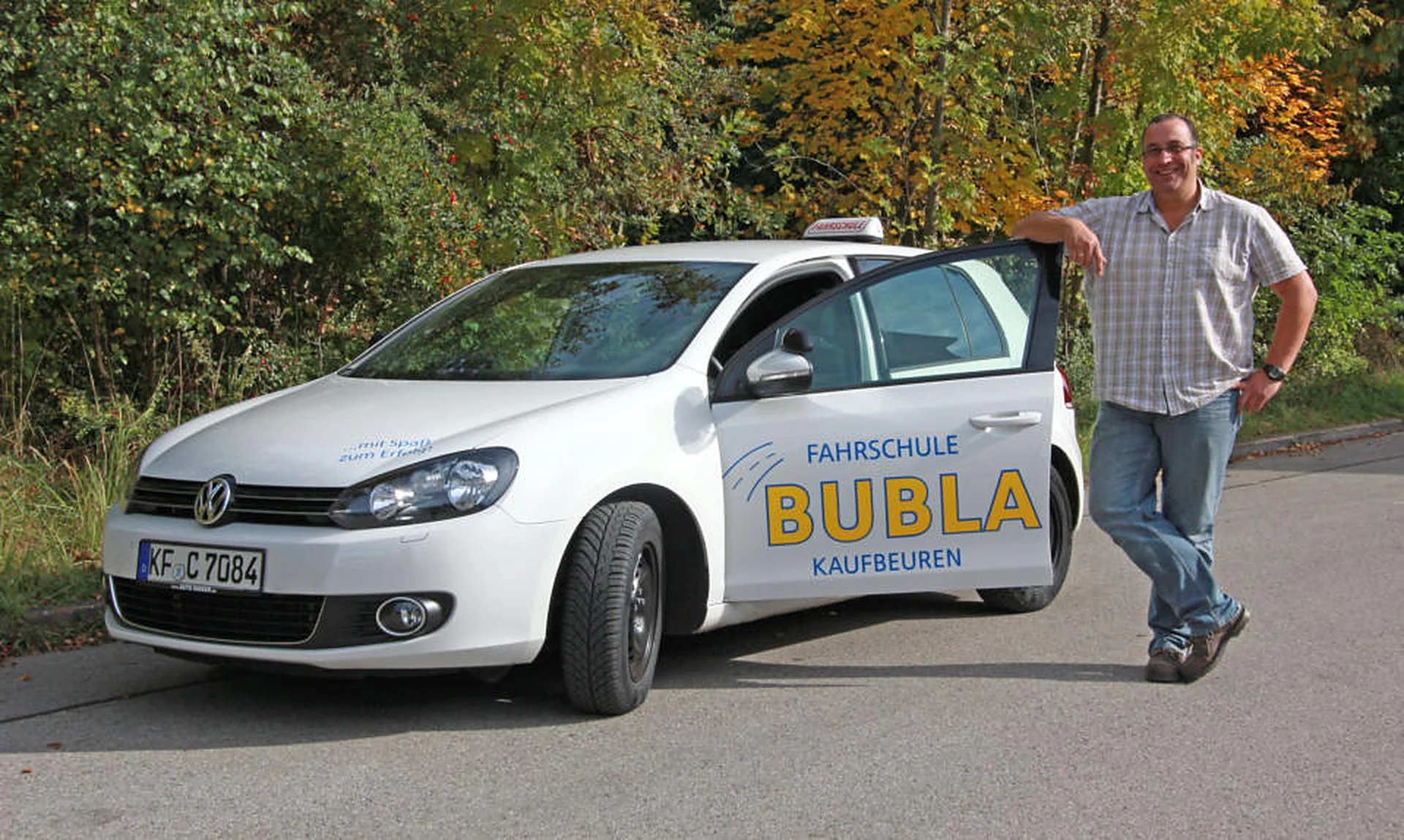 Fahrlehrer der Fahrschule Bubla am weißen Fahrschul-Golf mit Bubla-Beschriftung