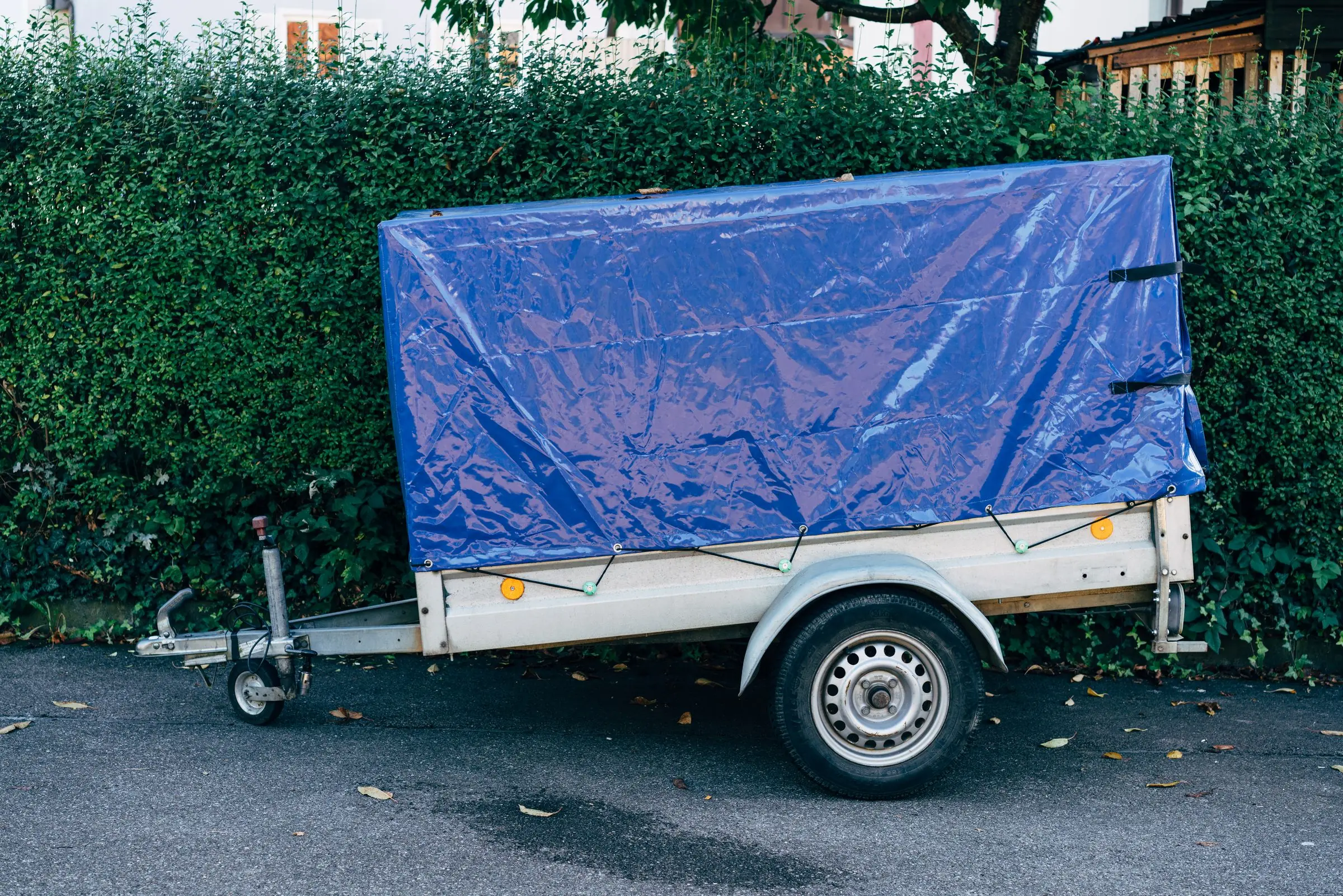 Pkw-Anhänger mit blauer Plane am Straßenrand