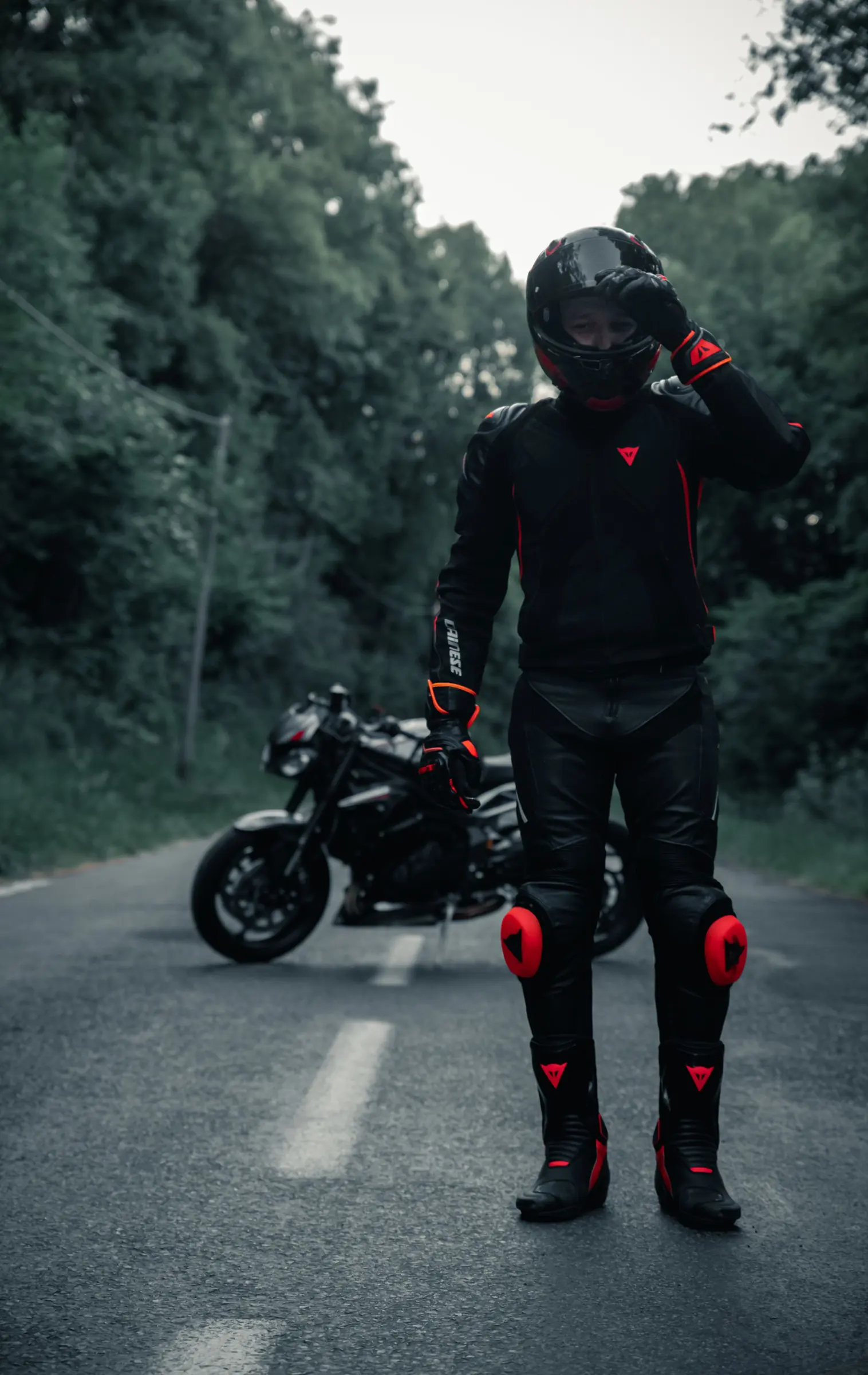 Motorradfahrer mit Helm steht vor seinem Motorrad auf einer Waldstraße